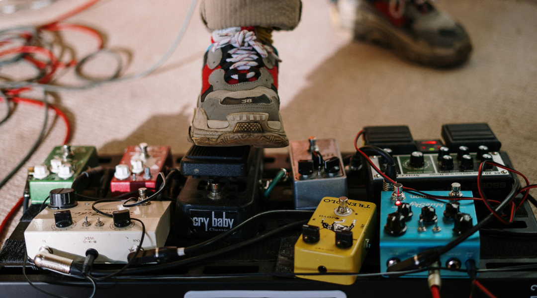 Foto eines Pedalboards mit Effektgeräten und einem Fuß, der auf ein Wah-Pedal drückt.