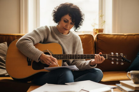 Gitarristin auf dem Sofa beim kreativen Songwriting.