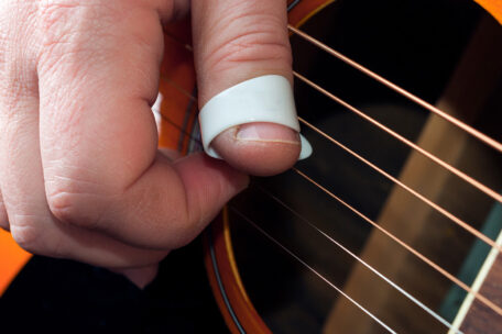 Rechte Hand eines Gitarristen beim Spielen mit Daumenpick auf einer Westerngitarre.