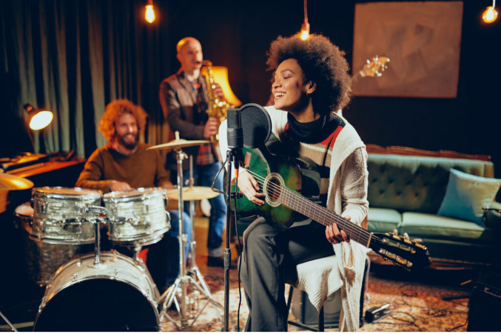 Singende Frau mit Gitarre, Mikrofon und Band im Hintergrund