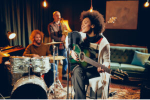 Singende Frau mit Gitarre, Mikrofon und Band im Hintergrund